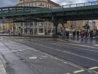 people wait to cross the street with their cars and people walking underneath the bridge as a pedestrian is crossing the street below