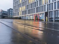 a wet street in the evening with a red light and building lights on it,