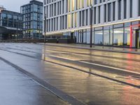 a wet street in the evening with a red light and building lights on it,