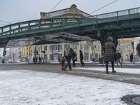 people walk under a bridge in the snow near a sidewalk and traffic light in front of it