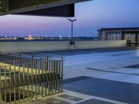 stairs to the roof of an airport building with city lights in background at dusk from elevated parking area