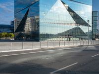 the reflection of mountains is shown in this glass skyscraper that reflects the surrounding buildings along a street