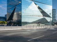 the reflection of mountains is shown in this glass skyscraper that reflects the surrounding buildings along a street