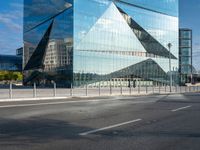 the reflection of mountains is shown in this glass skyscraper that reflects the surrounding buildings along a street