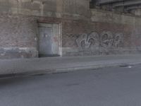 a brick building covered in graffiti next to an empty street way in front of it