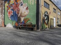 some murals on the side of an old building and a bench that is next to it