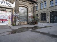 an old brick building with lots of graffiti on the side of it and puddles of water