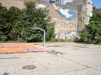 an abandoned street with a mural on it's side, near trees and a basketball court