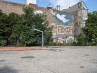 an abandoned street with a mural on it's side, near trees and a basketball court