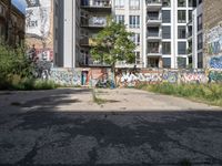 a street has a building with graffiti on it, and green grass in the foreground