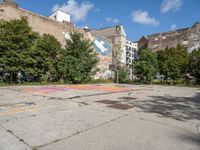 an empty asphalt ground with a graffiti filled parking lot, in front of some buildings and trees