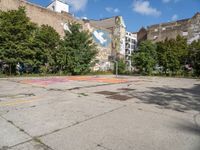 an empty asphalt ground with a graffiti filled parking lot, in front of some buildings and trees