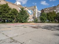 an empty asphalt ground with a graffiti filled parking lot, in front of some buildings and trees