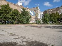 an empty asphalt ground with a graffiti filled parking lot, in front of some buildings and trees