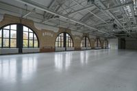 a large hall with three windows and concrete floors and high ceilings and lots of windows