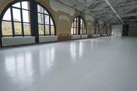 a large hall with three windows and concrete floors and high ceilings and lots of windows