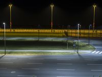 a street at night in the distance with poles and lights on it and grass at the edge