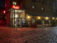 the outside of a hotel with a neon sign next to a cobblestone sidewalk