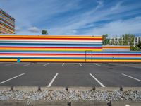 an empty parking lot painted brightly stripes on the wall of the building and sky as well as stones