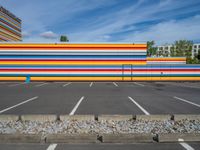 an empty parking lot painted brightly stripes on the wall of the building and sky as well as stones