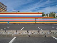 an empty parking lot painted brightly stripes on the wall of the building and sky as well as stones