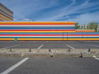 an empty parking lot painted brightly stripes on the wall of the building and sky as well as stones