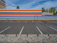 an empty parking lot painted brightly stripes on the wall of the building and sky as well as stones