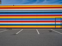 an empty parking lot painted brightly stripes on the wall of the building and sky as well as stones