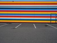 an empty parking lot painted brightly stripes on the wall of the building and sky as well as stones