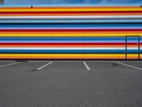 an empty parking lot painted brightly stripes on the wall of the building and sky as well as stones