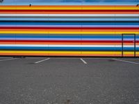 an empty parking lot painted brightly stripes on the wall of the building and sky as well as stones