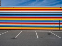 an empty parking lot painted brightly stripes on the wall of the building and sky as well as stones