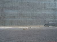 an empty bench sitting next to a large concrete building behind it with red bricks on either side