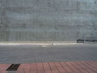 an empty bench sitting next to a large concrete building behind it with red bricks on either side