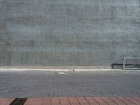 an empty bench sitting next to a large concrete building behind it with red bricks on either side