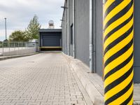 a bright yellow and black striped pole standing in front of a building next to a parking space