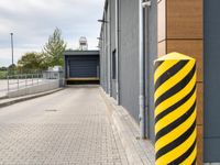 a bright yellow and black striped pole standing in front of a building next to a parking space