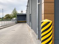 a bright yellow and black striped pole standing in front of a building next to a parking space