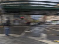 a blurry view of an intersection with a pedestrian crossing sign under a bridge above