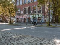 a red motorcycle parked next to a red brick building with graffiti on the side of it