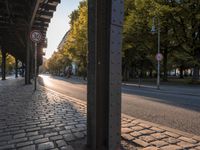 a street with a metal pole on the corner with trees and a sky background in it