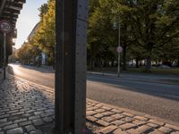 a street with a metal pole on the corner with trees and a sky background in it