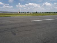 an empty road with some white clouds in the sky near the air traffic control tower