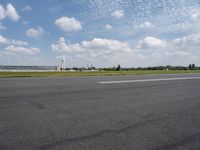 an empty road with some white clouds in the sky near the air traffic control tower