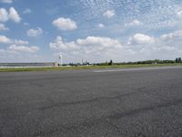 an empty road with some white clouds in the sky near the air traffic control tower