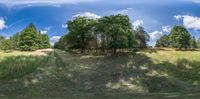 this is a panoramic photograph of a field with trees and blue sky in the background