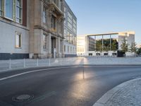 an empty street in front of a big building near the city street is surrounded by barbed wire