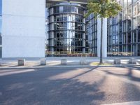 the modern building has an entrance and glass facade, along with bench seating, trees, and a street with lots of windows