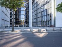 the modern building has an entrance and glass facade, along with bench seating, trees, and a street with lots of windows