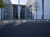 the modern building has an entrance and glass facade, along with bench seating, trees, and a street with lots of windows